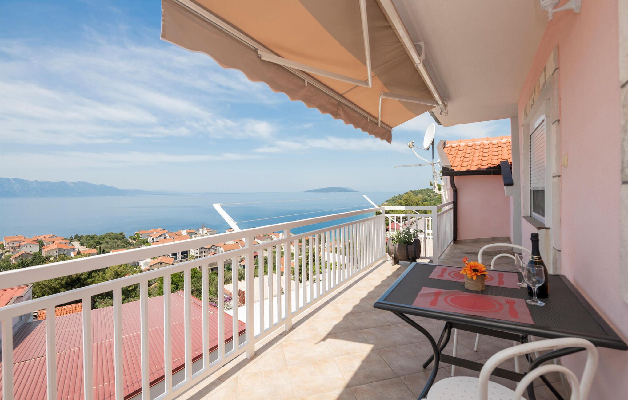 A balcony with a table set for two, overlooking a coastal view.