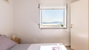 A bedroom with a bed, a nightstand, a lamp, a window with a view of the beach, and a door. - 1 bedroom awesome apartment in Podaca (Podaca)