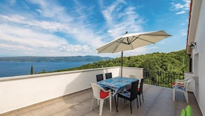 Un balcone con tavolo e sedie, un ombrellone grande e vista mare e montagne.
