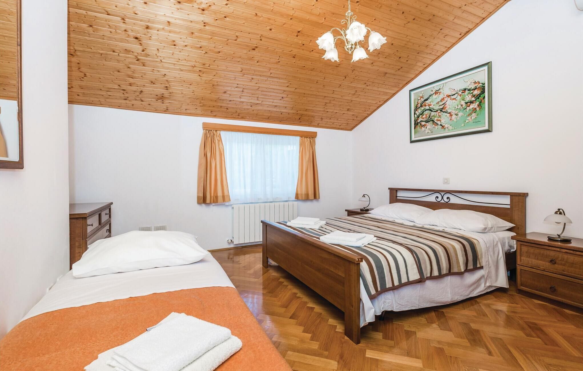 A bedroom with a wooden ceiling, a bed with striped bedding, a nightstand, a dresser, a window with curtains, and a painting on the wall.
