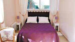 Un dormitorio con una cama grande, dos mesitas de noche con lámparas, una silla y una ventana con cortinas.