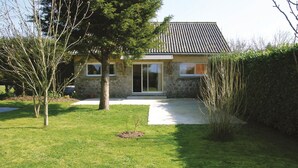 Una casa de piedra con techo de tejas, una puerta principal y un pequeño jardín delantero con un árbol y césped.