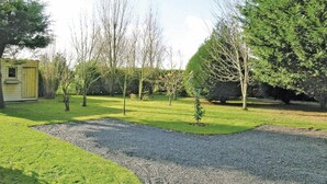 Un jardín bien cuidado con un camino de grava, un cobertizo pequeño y varios árboles.