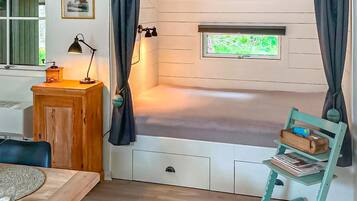 A room with a bunk bed, a desk with a lamp, a chair, and a window with curtains.