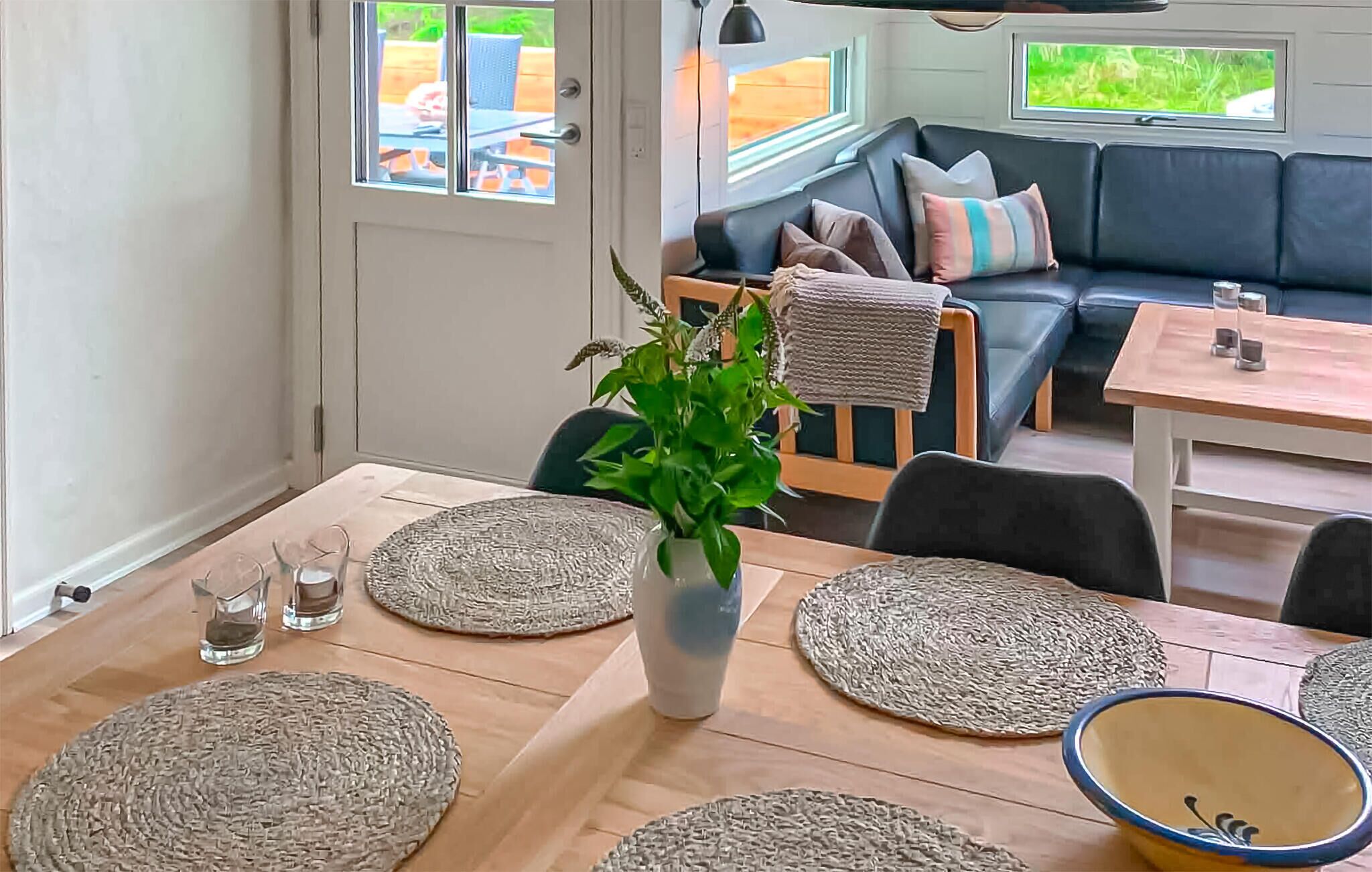 A cozy interior with a dining area featuring a wooden table, woven placemats, and a central potted plant.