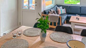 A cozy interior with a dining area featuring a wooden table, woven placemats, and a central potted plant.