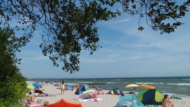 Een strandzicht met tenten, parasols en mensen die ontspannen op het zand.