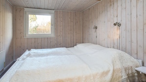 A bedroom with a large bed, wooden walls, a window, and a small bedside table. - Cozy home in Løkken with sauna (Løkken)