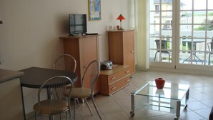 A room with a dining table, chairs, a TV, a cabinet, and a window with a view of the outside. - House Baltic - Apartment no.: 7 (Sellin)
