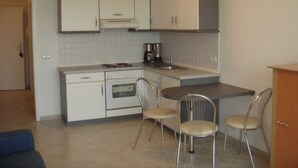A compact kitchen with white cabinets, a coffee maker, and two metal chairs. - House Baltic - Apartment no.: 7 (Sellin)