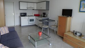 A compact living space with a kitchenette, a sofa, a glass coffee table, and a TV on a cabinet. - House Baltic - Apartment no.: 7 (Sellin)