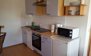 Una cocina compacta equipada con lavavajillas, horno, microondas y un refrigerador pequeño. Cuenta con una encimera de madera, un lavamanos y una repisa con un tazón y una tetera.