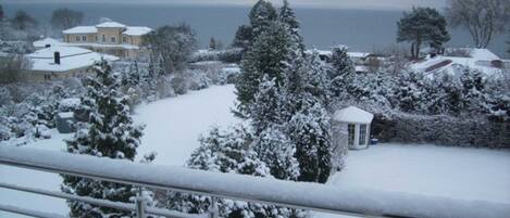 Ein Wohngebiet mit schneebedeckten Häusern und Bäumen, einem kleinen weißen Gazebo und Blick auf das Meer.