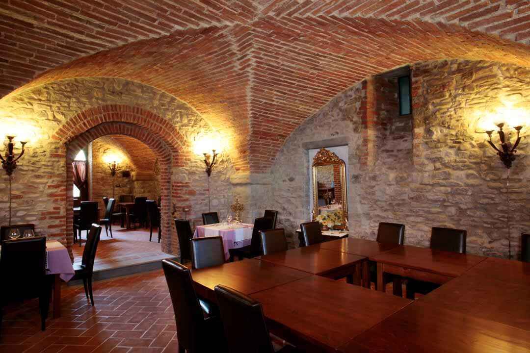 A dining area with a brick ceiling and stone walls, featuring tables and chairs arranged for dining.