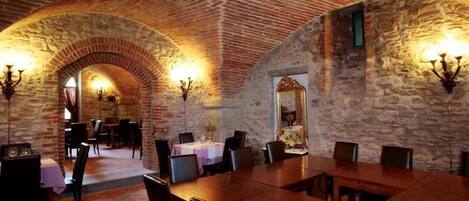 A dining area with a brick ceiling and stone walls, featuring tables and chairs arranged for dining.