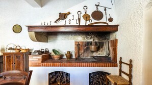 A rustic kitchen with a brick fireplace, wooden shelves with kitchen utensils, and a wooden chair. - Amazing home in Capannoli PI with WiFi (Capannoli PI)