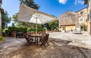 An outdoor patio with a table and chairs under a large umbrella, surrounded by potted plants and a rustic building in the background. - Amazing home in Capannoli PI with WiFi (Capannoli PI)