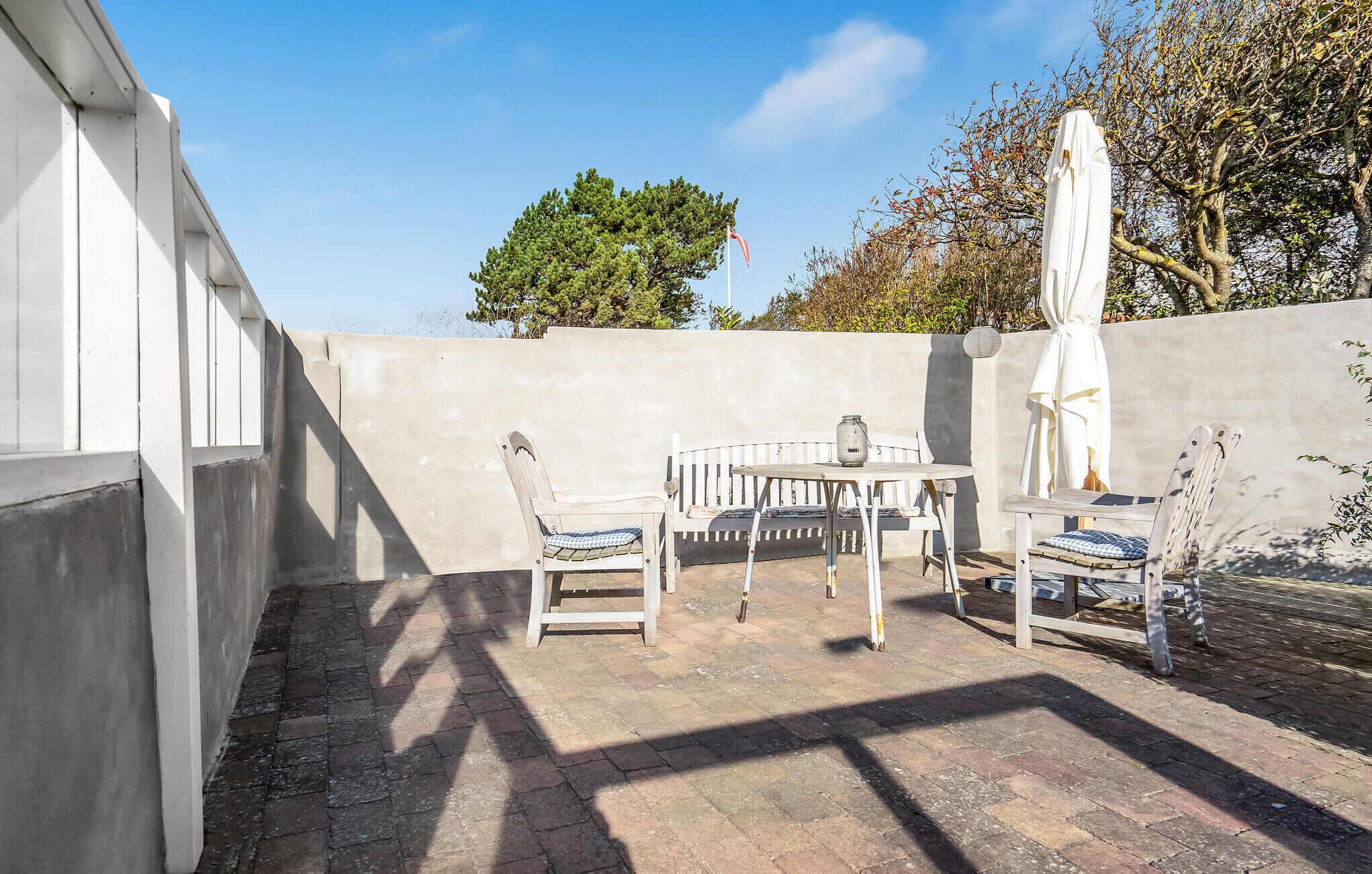 Une terrasse avec une table et deux chaises, un parasol blanc et un arbre en arrière-plan.