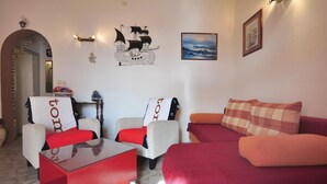 Ein Wohnzimmer mit einem roten Couchtisch, zwei Sesseln, einem Sofa und einer Wand mit Kunstwerken und einem gerahmten Bild.