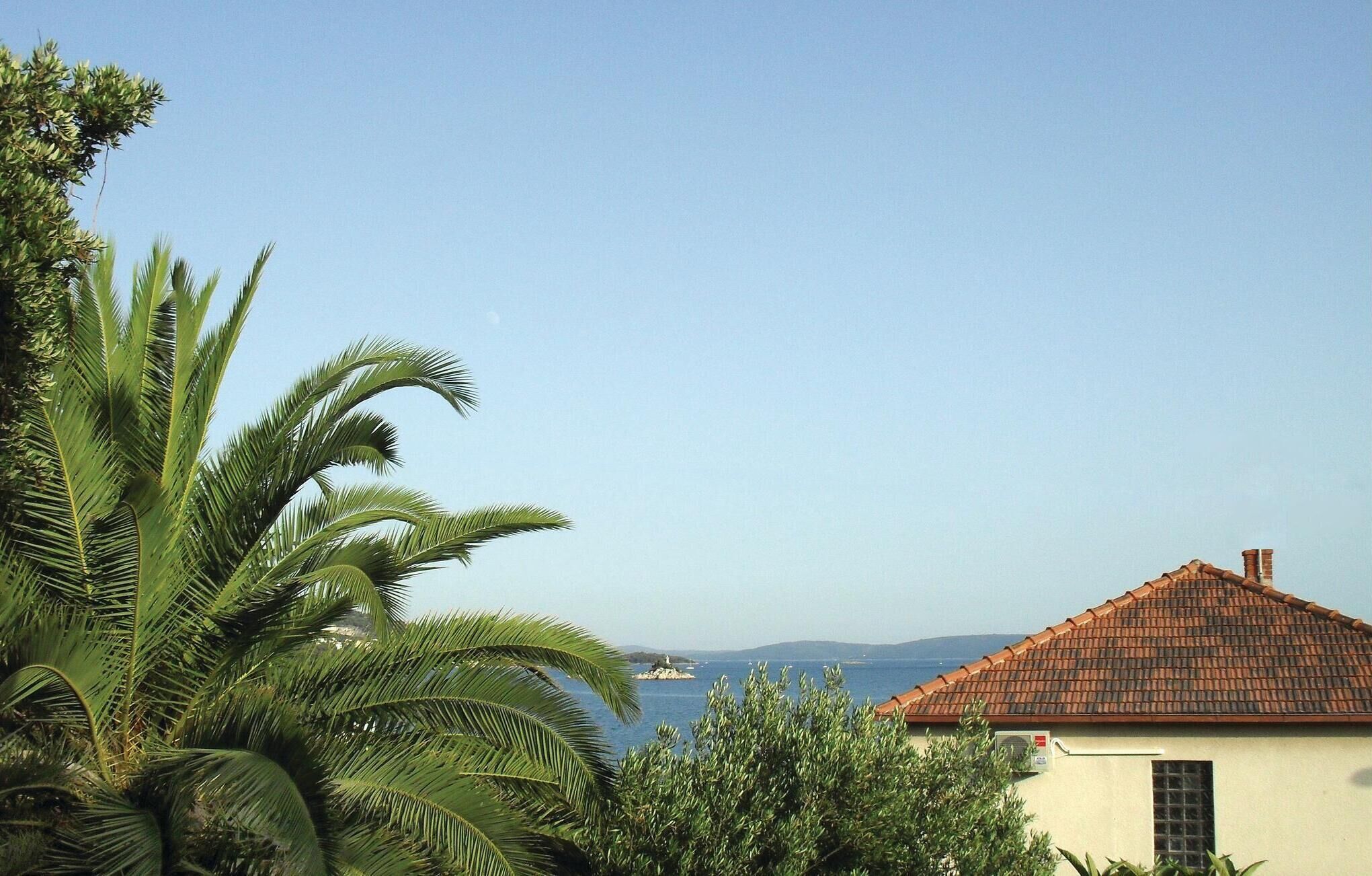 Un bâtiment situé sur la côte, doté d’un toit recouvert de tuiles, d’une cheminée bien visible et offrant une vue sur la mer et les collines lointaines.