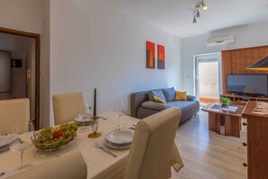 Relax in this stylish living space with a dining area, featuring a sofa, dining table for two, and a mounted television.