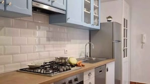 Una cocina con armarios blancos, estufa a gas, lavamanos y refrigerador.