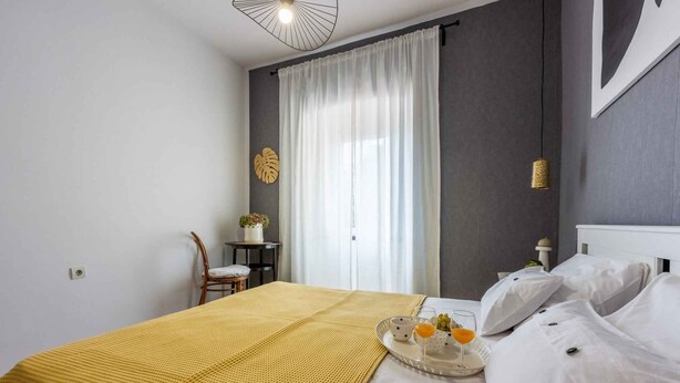Habitación de hotel con una cama, una mesita de noche con una bandeja de desayuno, una silla y un ventanal con cortinas.