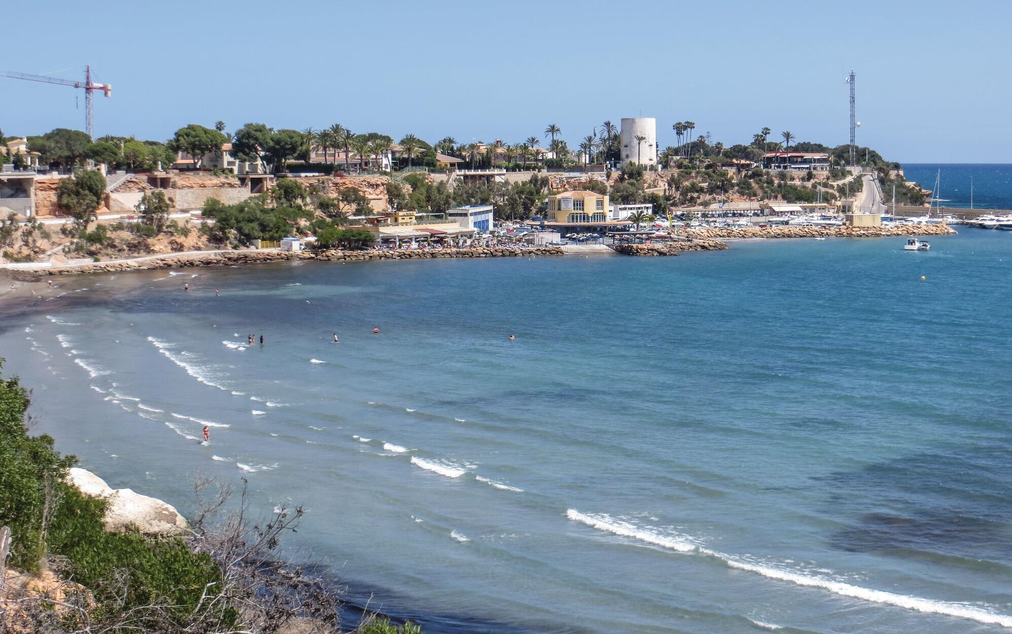 Un pueblo costero con una playa, costa rocosa y edificios con balcones que dan al mar.