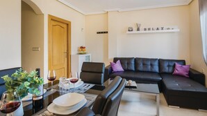Un soggiorno moderno con un divano in pelle nera, un tavolo da pranzo per due persone e un angolo cottura con un'esposizione di frutta.