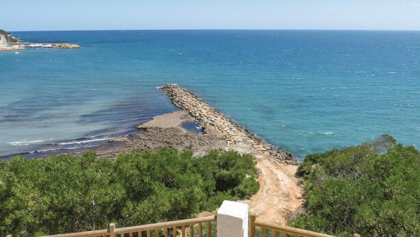 Una vista costiera con un molo roccioso che si protende verso il mare, circondato dal verde.