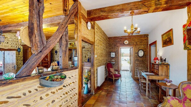 Un intérieur rustique avec des poutres apparentes, un mur en pierre, un sol carrelé et un lustre.