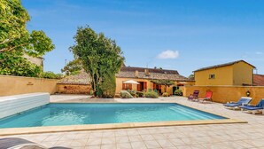Une piscine dont le fond est recouvert de carrelage, entourée de chaises longues et bordée d’un bâtiment dont le toit est également recouvert de tuiles.