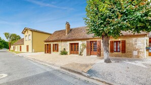 Un bâtiment traditionnel en pierre, avec un toit en tuiles, des volets en bois et une rue pavée devant.