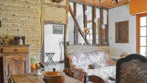 Une pièce rustique avec des poutres apparentes, une table en bois surmontée d’un pot, un canapé à motifs floraux et un mur de briques orné d’un décor.