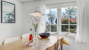 Ein Essbereich mit einem Tisch für vier Personen, einer Pendelleuchte, einem Fenster mit Vorhängen und einem gerahmten Bild an der Wand.