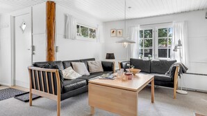 Ein modernes Wohnzimmer mit einem schwarzen Ledersofa, einem Holztisch und einem großen Fenster mit weißen Vorhängen.