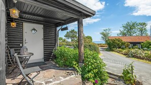 Eine Holzhütte mit einer Steinterrasse, einer Tür mit Fenster und Blick auf das Meer.