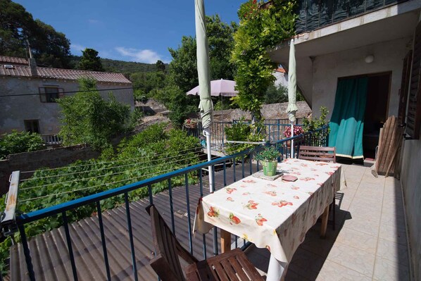 A balcony with a table set for dining, surrounded by greenery and a view of a village.