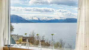 Une vue depuis une fenêtre donnant sur un lac paisible, avec des montagnes enneigées en arrière-plan.