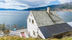 Une maison blanche avec un toit en pente, une cheminée et une vue sur un lac et des montagnes.