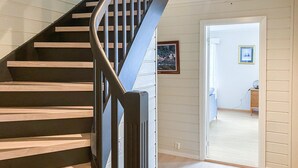 Un escalier en bois avec une rampe métallique mène à une pièce où se trouvent un lit, une commode et un tableau encadré au mur.