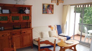 A cozy living room with a wooden cabinet, a sofa, a dining table, and a balcony with a view of greenery. - Gorgeous apartment in Argeles sur Mer (Argeles sur Mer)