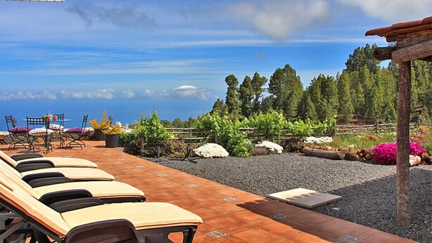 A terrace with sun loungers, a table with chairs, and a view of the ocean and trees. - El Topo, Puntagorda, Spain (Puntagorda)