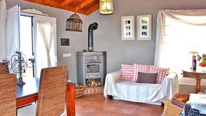 A cozy living room with a fireplace, a dining table with wicker chairs, a sofa with checkered pillows, and a wall-mounted picture frame. - El Topo, Puntagorda, Spain (Puntagorda)