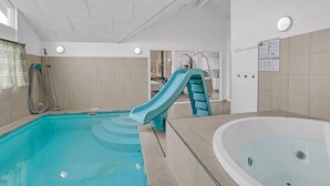 A swimming pool with a slide, a separate hot tub, and a shower area.