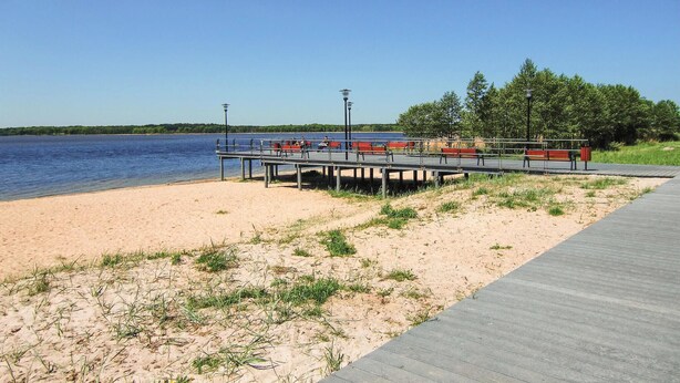 A beach with a wooden walkway and red benches along the water's edge. - Cozy home in Nowe Warpno with ethernet internet (Nowe Warpno)