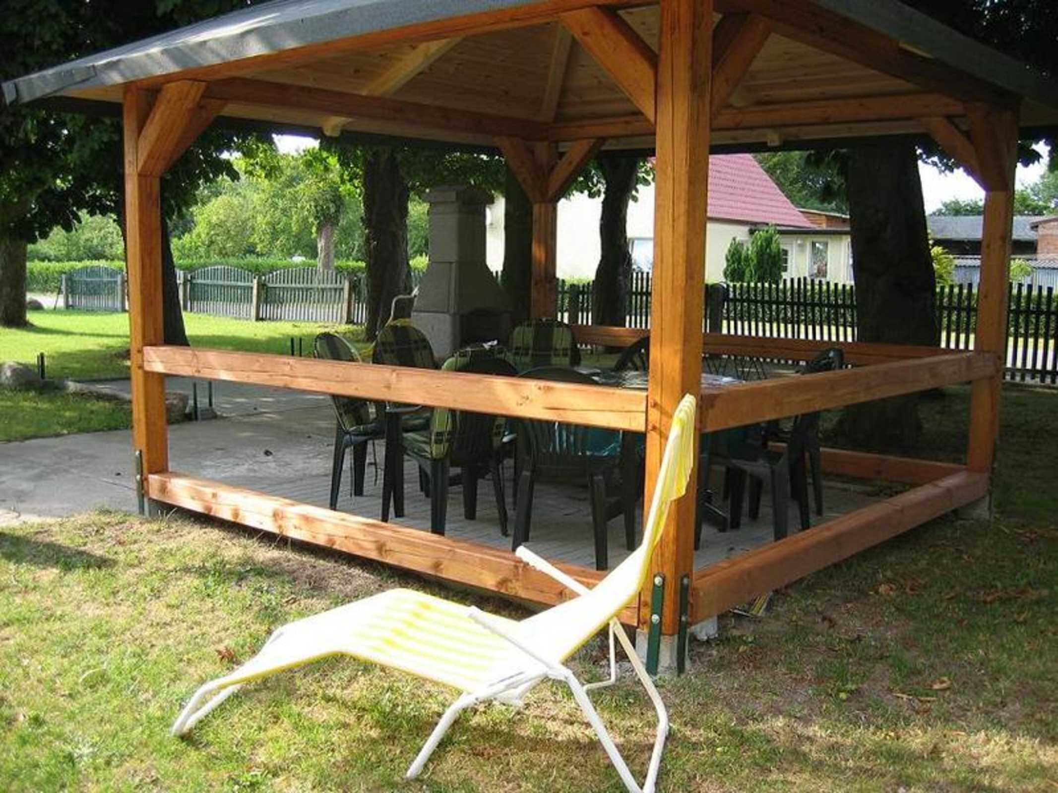 Um pavilhão de madeira com área de estar coberta, incluindo uma mesa e cadeiras.