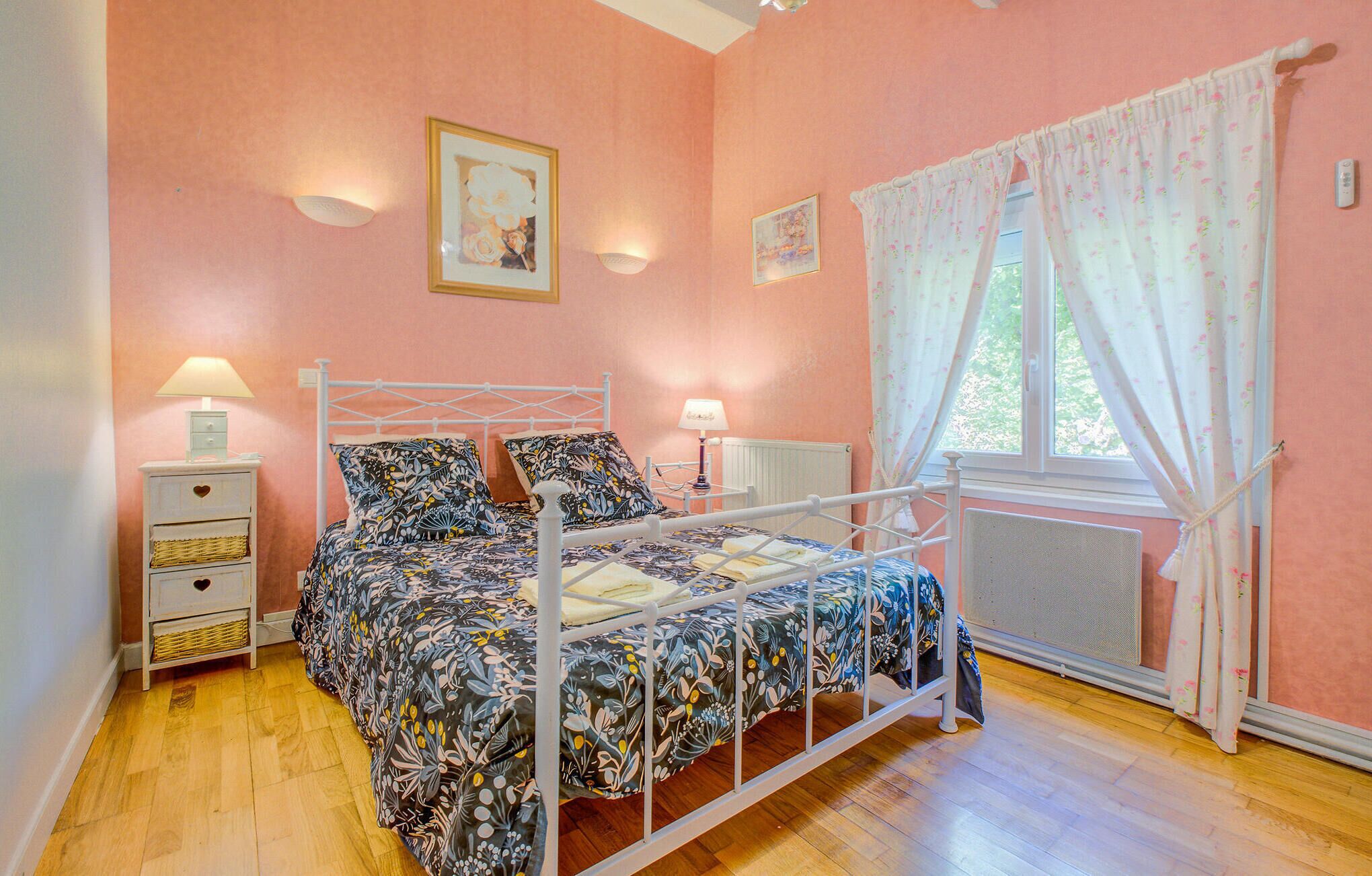 A bedroom with a four-poster bed, two bedside tables, a radiator, and a window with curtains.