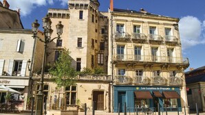 Un bâtiment historique doté d’une tour, un café avec une terrasse, et une façade bleue ornée d’une enseigne.