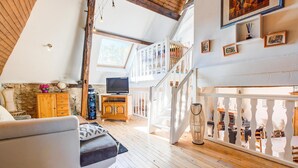 Un loft spacieux avec de hauts plafonds, des poutres apparentes, un escalier, une télévision et une cheminée.
